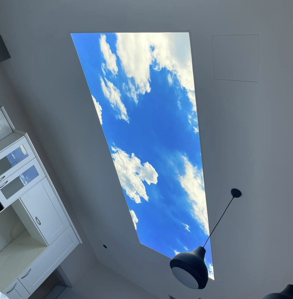 Recessed illuminated stretch ceiling with realistic blue sky and cloud print installed in a modern villa kitchen at The Villa Dubai. The 6500K daylight lighting creates a natural sky effect and visually expands the interior space. Recessed illuminated stretch ceiling with realistic blue sky and cloud print installed in a modern villa kitchen at The Villa Dubai. The 6500K daylight lighting creates a natural sky effect and visually expands the interior space.