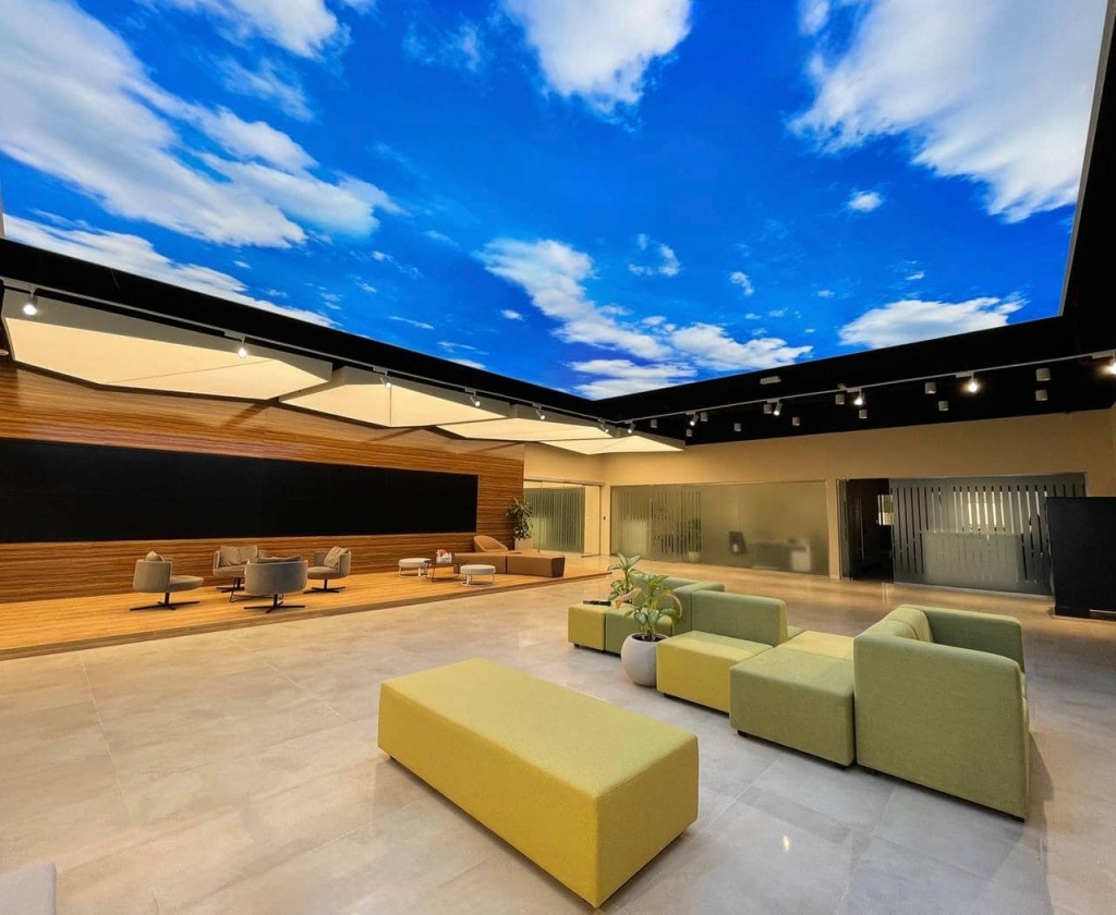 Large suspended lightbox ceiling with realistic sky print and integrated 6500K LED lighting in a modern office interior in Sharjah. Large suspended lightbox ceiling with realistic sky print and integrated 6500K LED lighting in a modern office interior in Sharjah.