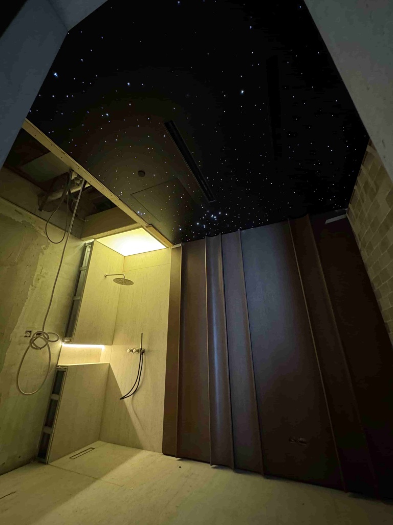 Black stretch ceiling with fiber optic star lighting creating a realistic night sky effect inside a luxury sauna at Al Barari. Black stretch ceiling with fiber optic star lighting creating a realistic night sky effect inside a luxury sauna at Al Barari.