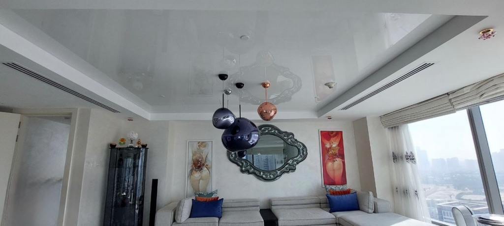 Premium white glossy stretch ceiling integrated into a luxury living and dining area with panoramic skyline views. Premium white glossy stretch ceiling integrated into a luxury living and dining area with panoramic skyline views.