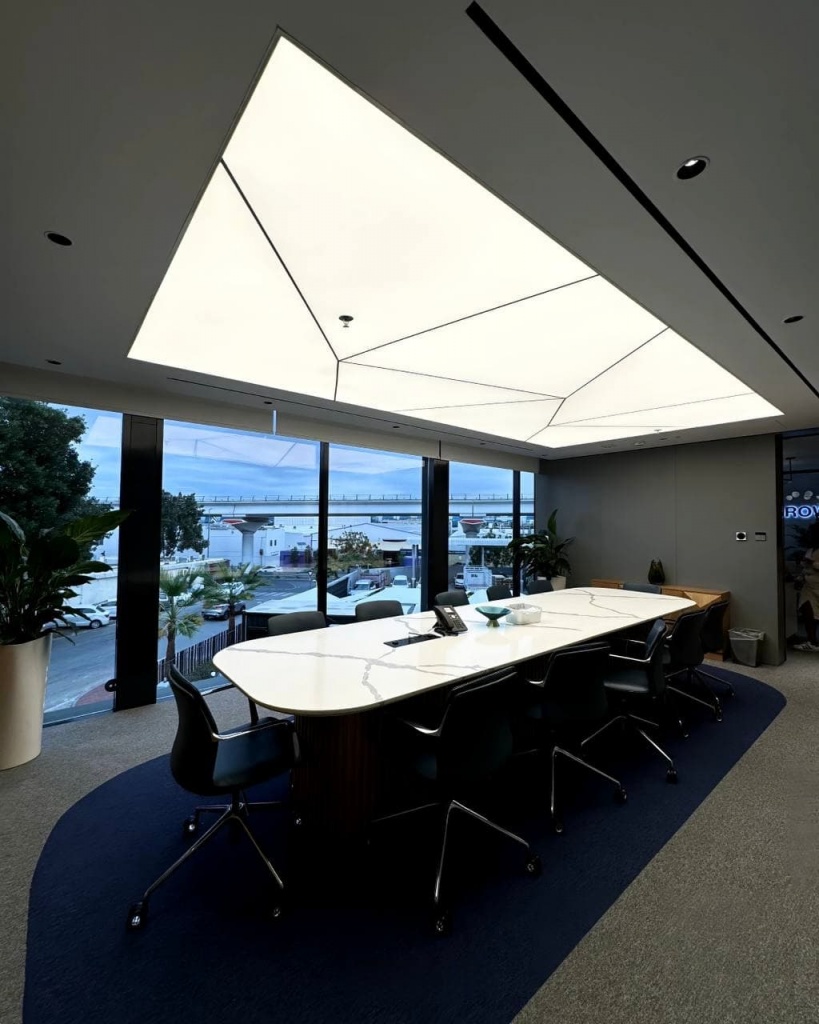 Modern luminous stretch ceiling with architectural black profile divisions creating a clean geometric design in a conference room. Modern luminous stretch ceiling with architectural black profile divisions creating a clean geometric design in a conference room.