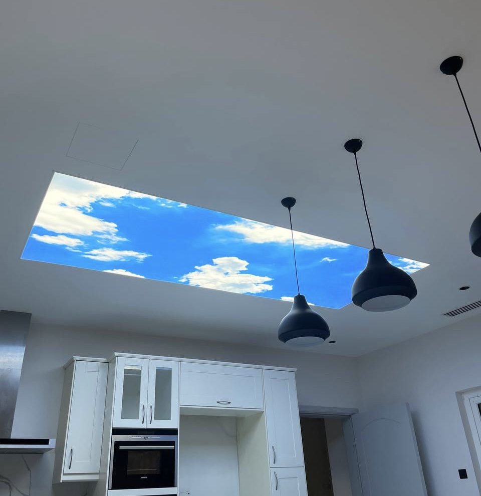 Custom translucent stretch ceiling with sky artwork and integrated LED illumination installed in a luxury villa kitchen at The Villa community. The ceiling creates the illusion of an open sky above the interior. Custom translucent stretch ceiling with sky artwork and integrated LED illumination installed in a luxury villa kitchen at The Villa community. The ceiling creates the illusion of an open sky above the interior.